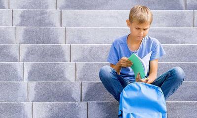 jongen met rugzak en boek op trap van school